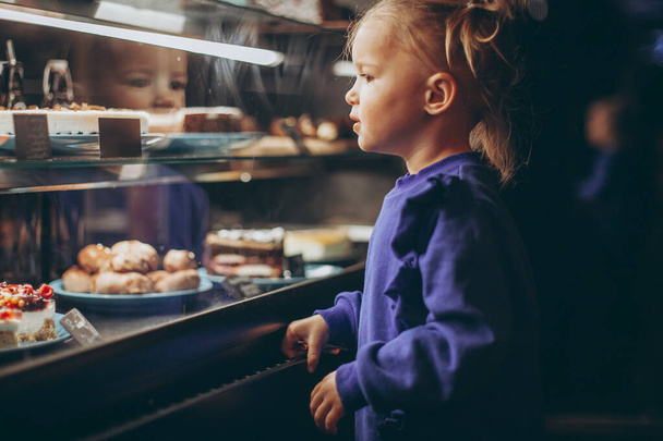 little pretty girl chooses pastries in a cafe. a child next to a showcase with goods - Valokuva, kuva