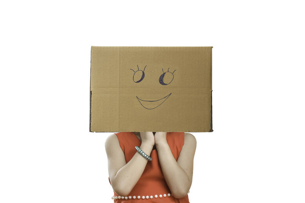 Маленькая девочка с картонной коробкой на голове с смайликом на белом фоне. - Фото, изображение