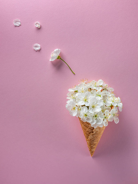pose plate de fleurs de cerisier blanc dans un cône de gaufre avec des pétales volants avec un fond rose espace négatif
 - Photo, image