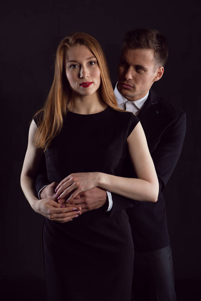 A sexy man looks in amazement at a beautiful red haired girl who has his arm around her waist - Фото, изображение