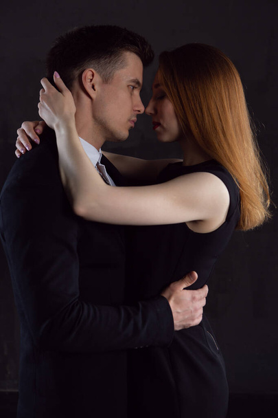 A gorgeous girl in a black dress closes her eyes with pleasure and gently embraces her cute man before a passionate kiss. relationships between men and women - Valokuva, kuva
