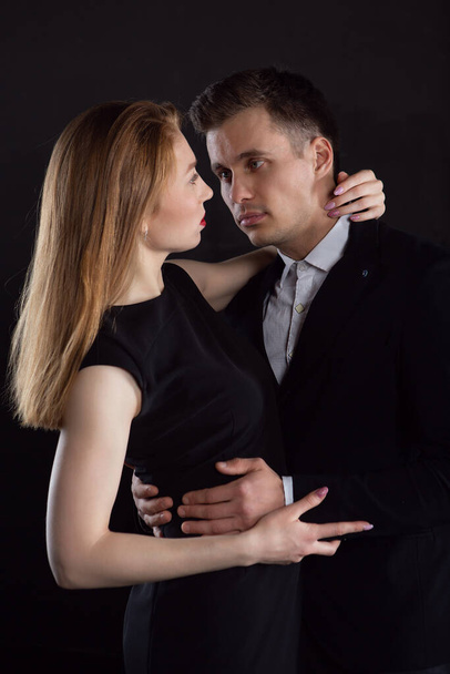 A beautiful young girl gently embraces a man who looks into her eyes tenderly by the neck and he gently holds her by the waist. Sexy couple before a kiss - Fotografie, Obrázek