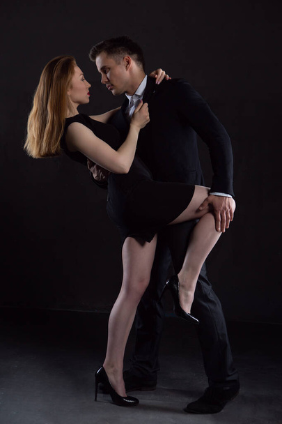 A man in an elegant black suit holds a sexy girl who is embracing him behind his back - Foto, Imagen