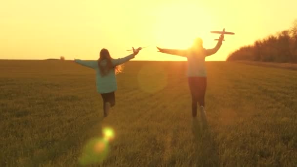 Sogni di volare. Concetto infanzia felice. Due ragazze giocano con un aereo giocattolo al tramonto. Bambini sullo sfondo del sole con un aereo in mano. Silhouette di bambini che giocano in aereo - Filmati, video