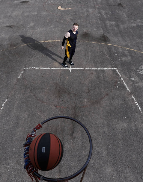 Dışarıda, uzun gölgeli spor alanında basketbol oynayan genç bir adam. - Fotoğraf, Görsel