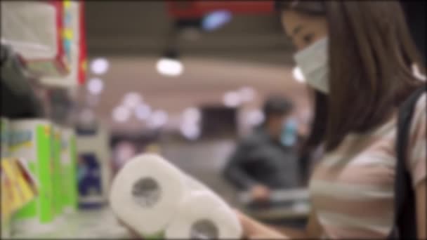 Jonge Aziatische vrouw in masker bij het kiezen van toiletpapier rolpapier in de supermarkt tijdens covid-19 crisis, voorraad op voorraad, corona virus wereldwijde pandemie, virus verspreiding preventie 4k, BLUR schot - Video