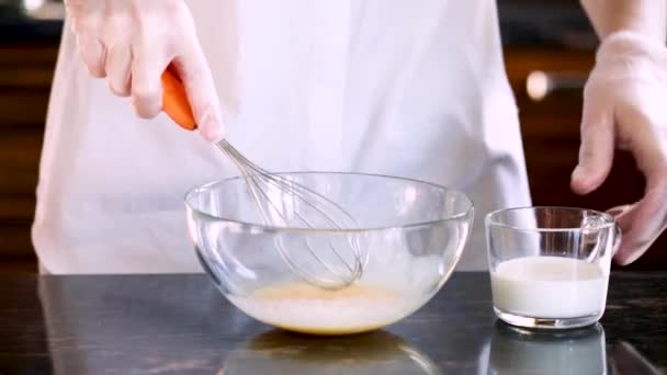 Le mani guantate delle donne sbattono le uova in una ciotola trasparente in cucina
 - Filmati, video