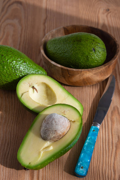 Aerial view of avocados, one cut and one blue knife, with selective focus, on wooden board, vertical - Photo, Image