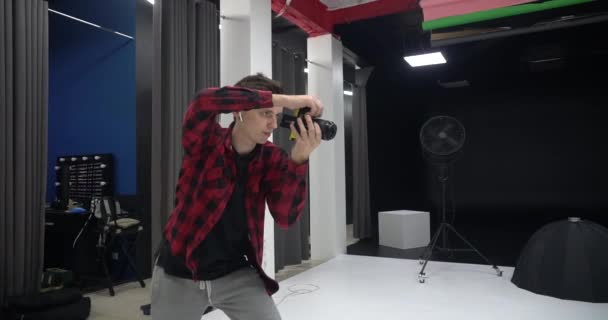 Jovem bonito fotógrafo profissional do sexo masculino tirar fotos de um modelo em um estúdio. Ele está satisfeito com as imagens capturadas. Câmera digital DSLR
. - Filmagem, Vídeo