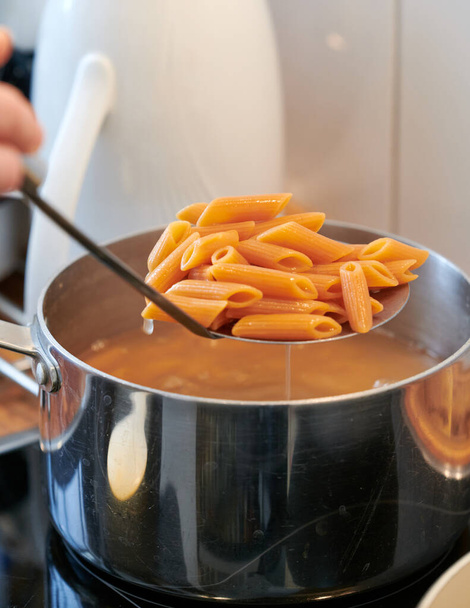 macarrão italiano sem glúten e vegan, com farinha de lentilha, enquanto é drenado do pote na cozinha
 - Foto, Imagem