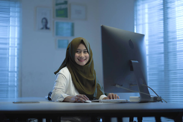  beautiful young Muslim Asian wearing green headscarves, in work from home modern interior design coworking space with computer, keyboard, and monitor - Foto, afbeelding