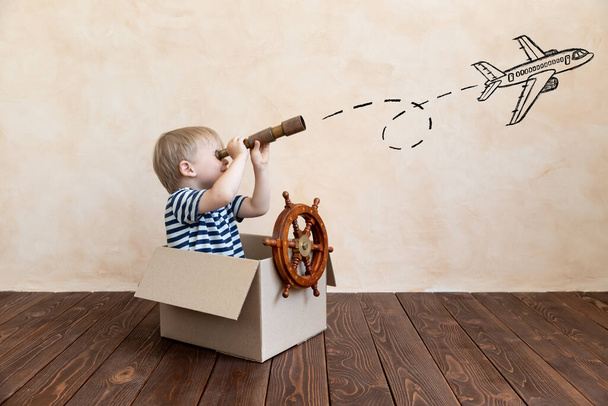 Happy child dreams of becoming a captain. Kid having fun at home. Boy wearing striped shirt playing in cardboard box. Summer vacation and travel concept. Dream and imagination - Foto, Imagem