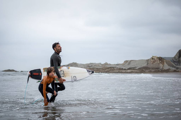 SOPELA, SPAIN - Aug 24, 2019: Father and son returning from surfing - 写真・画像