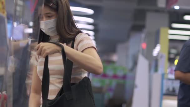 Nuori aasialainen nainen suojelevassa naamiossa kassalla, ruokakaupan hygienia, ruoan varastointi covid-19-koronaviruksen aikana, maailman pandemian aiheuttama talouskriisi, taloudellinen ongelma
 - Materiaali, video