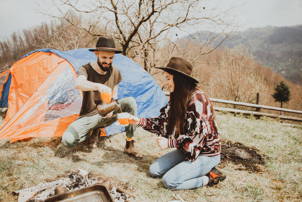 Loving couple sitting on the mountain outdoors. Man and woman travel together. Couple traveler enjoys nature, hugs, looks at the landscape near the tent - 写真・画像