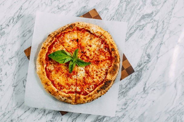 Italian pizza with mozzarella cheese and basil on a marble table - Фото, изображение