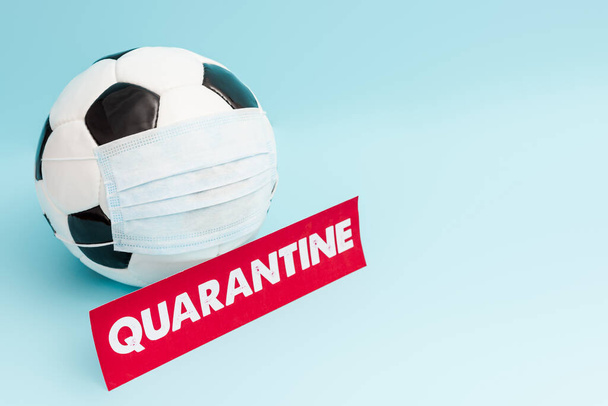 soccer ball in medical mask near paper with quarantine lettering on blue  - Foto, Bild