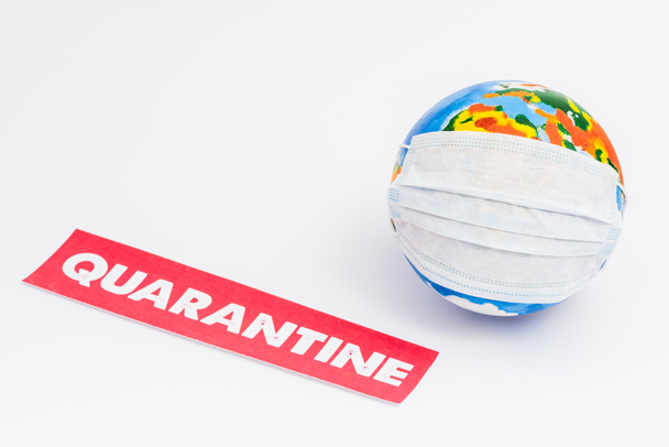 глобус в медицинской маске рядом с красной бумагой с карантинными надписями на белом с копировальным пространством
 - Фото, изображение