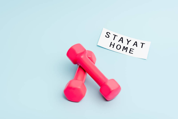 pink dumbbells near paper with stay at home lettering on blue with copy space - Foto, imagen