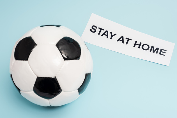 soccer ball near paper with stay at home lettering on blue - Fotoğraf, Görsel