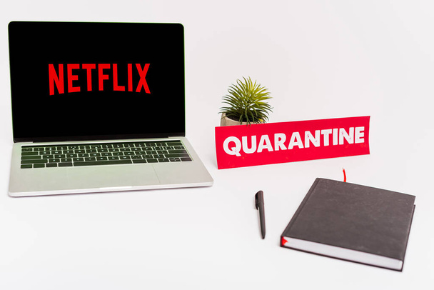 KYIV, UKRAINE - APRIL 8, 2020: laptop with netflix website on screen near plant, pen, notebook and paper with quarantine lettering on white  - Photo, Image