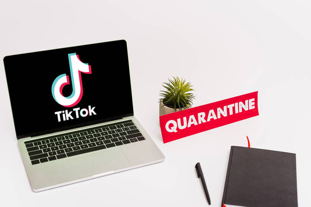 KYIV, UKRAINE - APRIL 8, 2020: laptop with tik tok website on screen near green plant, pen, notebook and paper with quarantine lettering on white  - Foto, imagen