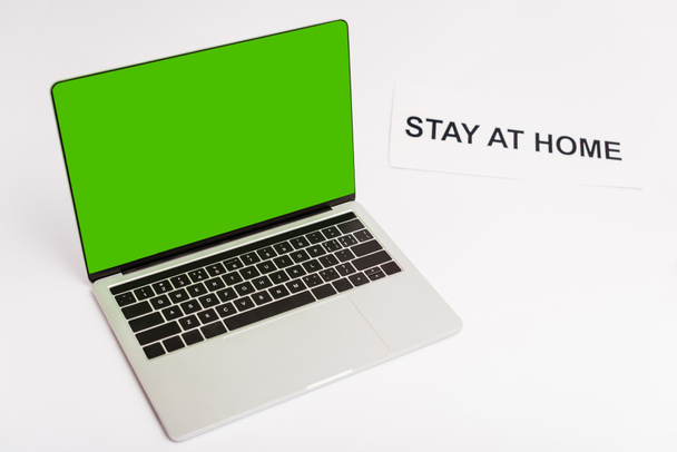 ordinateur portable avec écran vert près du papier avec rester à la maison lettrage sur blanc
  - Photo, image
