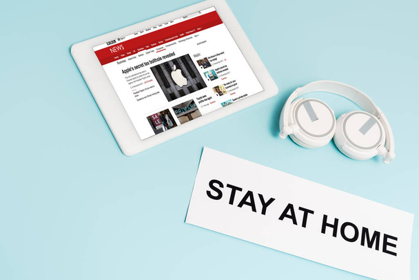 KYIV, UKRAINE - APRIL 8, 2020: digital tablet with bbc news app near headphones and paper with stay at home lettering on blue  - Fotografie, Obrázek