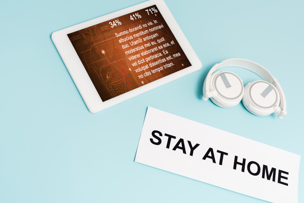 tableta digital con aplicación médica cerca de auriculares y papel con letras de estancia en casa en azul
  - Foto, Imagen