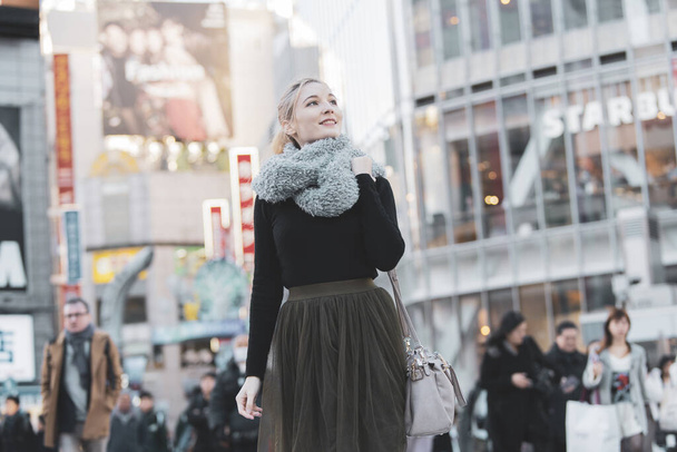 Young European woman sightseeing downtown Shibuya (Tokyo, Japan) with a smile - Foto, imagen