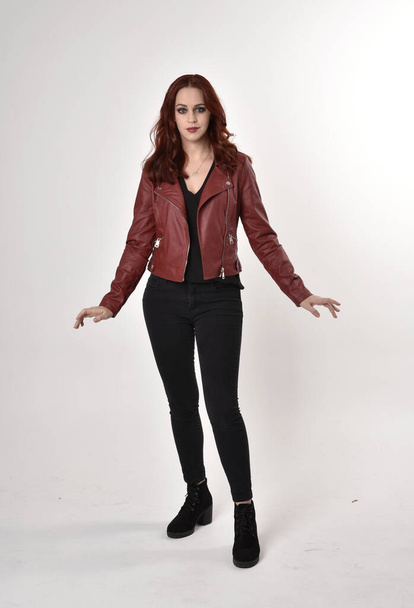 Retrato de uma menina bonita com cabelo ruivo vestindo calças de ganga pretas e botas com jaqueta de couro. comprimento total em pé pose em um fundo de estúdio
. - Foto, Imagem