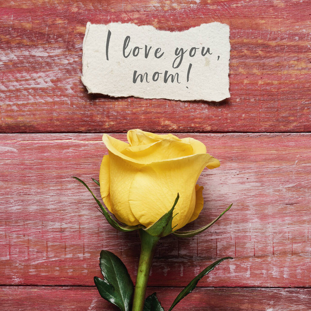 żółta róża i kartka papieru z napisem "Kocham cię mamo", na czerwonej rustykalnej drewnianej powierzchni. - Zdjęcie, obraz
