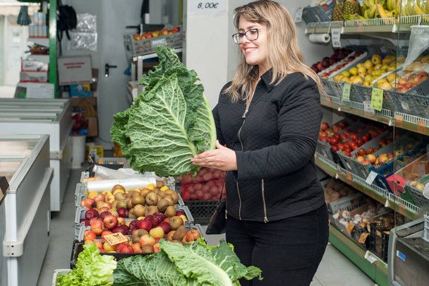 sorridente giovane donna bionda che tiene foglie di indivia in un negozio di alimentari
. - Foto, immagini