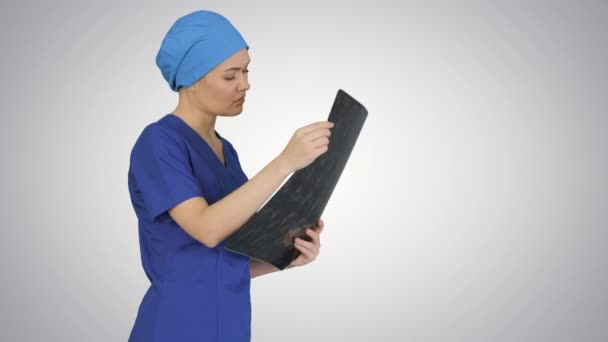 Serious female doctor looking at MRI scan of brain on gradient background. - Filmati, video