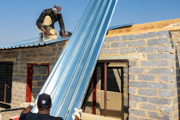 Soweto, South Africa - September 05, 2009: Diverse Community Outreach program helping to install metal roofing on a small affordable house in local township - Photo, image