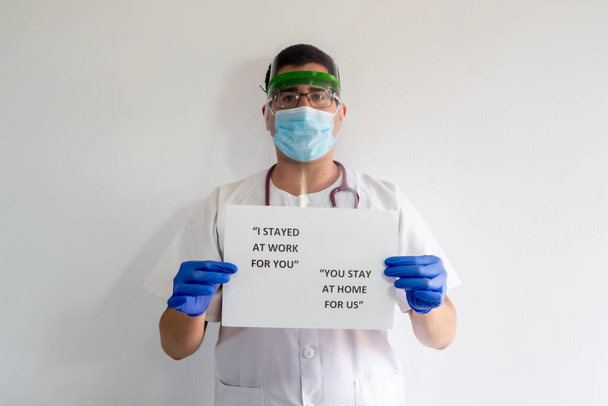 Infermiere di sesso maschile con protezione del viso, maschera, guanti e stetoscopio. Ha un cartello che dice "Sono rimasto al lavoro per te
". - Foto, immagini