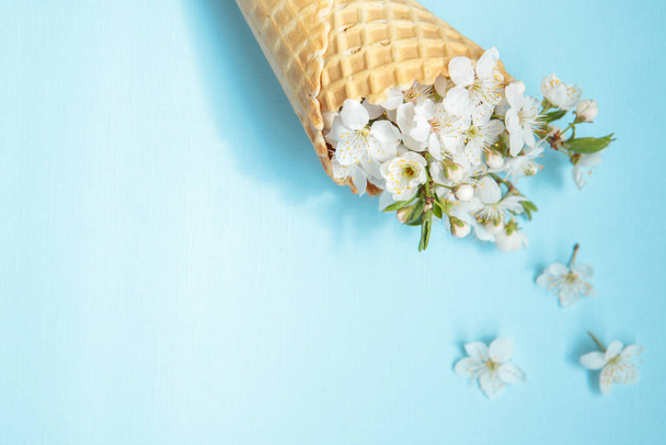 Ice cream cone with white flowers on a blue background. Minimal spring concept. Flat lay, floral background.Space for text - Photo, Image