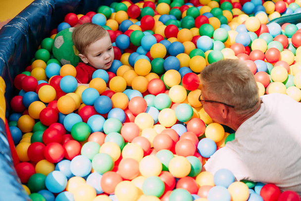 Щасливий смішний хлопчик 1-2 роки розважається з дідусем на вечірці на день народження в дитячому розважальному парку та ігровому центрі
.  - Фото, зображення