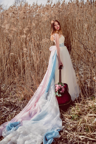 Schöne romantische europäische Mädchen mit Gitarre mit Blumen drinnen, posiert draußen. Konzept von Musik und Natur. Frühlingszeit. Mode retuschiert Schuss - Foto, Bild