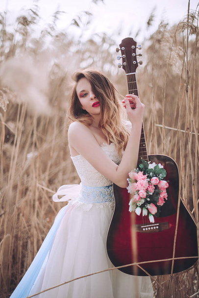 美しいロマンチックなヨーロッパの女の子の中の花とギター、屋外でポーズ。音楽と自然の概念。春の時間だ。ファッションレタッチショット - 写真・画像