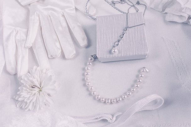 Białe akcesoria ślubne na tle ślubnym z perłami, białe satynowe wstążki i koronki, rękawiczki, bransoletka, płaski układ na blogu mody, widok z góry - Zdjęcie, obraz