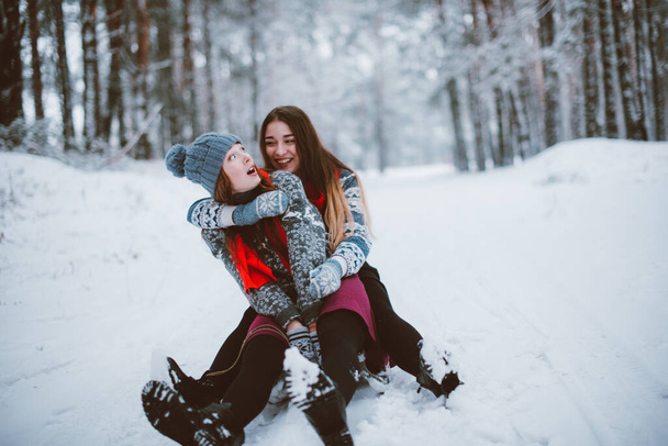 Two young teenage hipster girl friends together.Close up fashion portrait of two sisters hugs and having fun winter time,wearing sweater,best friends couple outdoors, snowy weather - 写真・画像