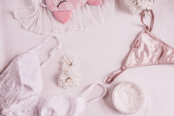 Flat lay for fashion blog and social media. Woman's glamour white and beige beauty accessories on a white background. Lingerie, jewelry, perfumes, cream, soap, panties, sleep mask, spiral hair ties. Copy space for text. - 写真・画像
