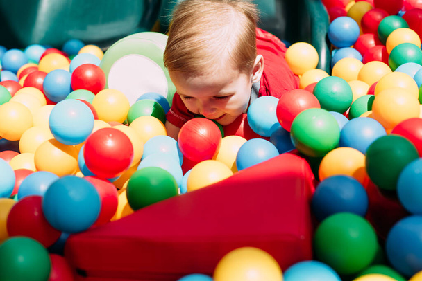 Boldog nevető fiú 1-2 éves szórakozás labda gödörben születésnapi party gyerekeknek vidámpark és beltéri játszóközpont. A gyerek színes labdákkal játszik a játszótéri labdarúgó medencében. Tevékenységi játékok kisgyereknek. - Fotó, kép