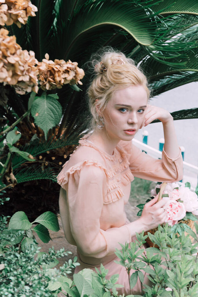 Smyslná mladá blondýna krásná roztomilá a elegantní žena na sobě růžová sedí na skále a dívá se do kamery přes tropické zelené džungle palmy pozadí v Číně. - Fotografie, Obrázek