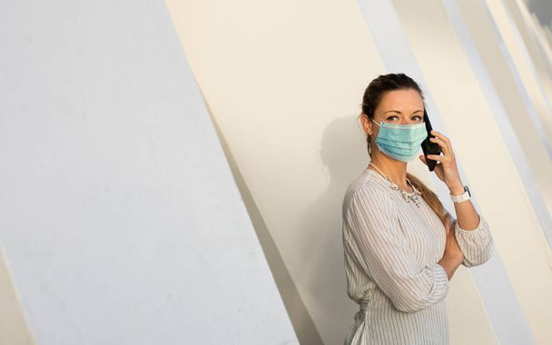 Fiatal, hivatásos nő telefonos üzleti ügyben, a Coronavirus Covid-19 egészségügyi válsága alatt. Egy üzletasszony arcmaszkot visel a fertőzés elkerülése érdekében.. - Fotó, kép