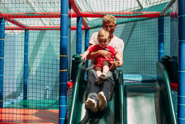 Buon ridere ragazzo 1-2 anni divertirsi con il nonno in festa di compleanno in parco giochi per bambini e centro giochi al coperto.  - Foto, immagini