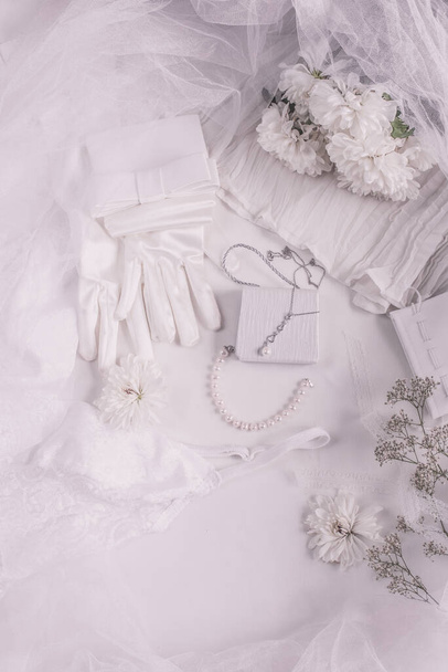 White bridal accessories for wedding background with pearls, white satin ribbons and lace, gloves, bracelet,flat lay for fashion blog, top view - Photo, Image