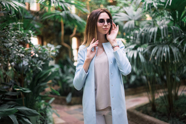 La giovane elegante ragazza positiva posa in un giardino botanico indossando giacca blu
. - Foto, immagini