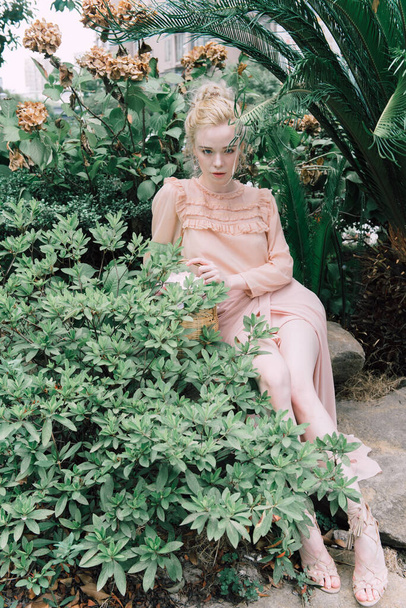 Sensual young blonde beautiful cute and elegant woman wearing pink sitting on the rock and looking into the camera over tropical green jungle palm background in China. - Foto, immagini